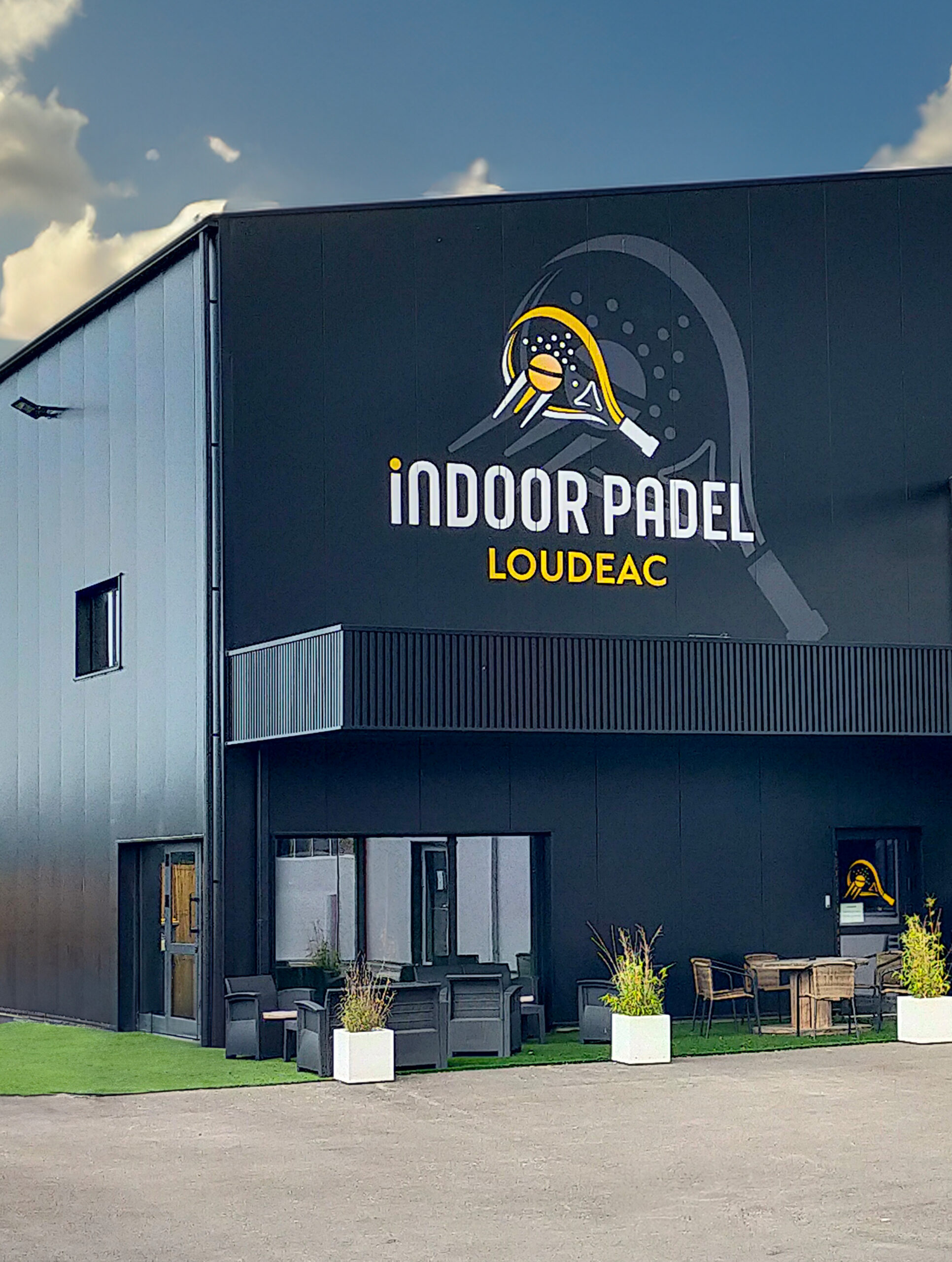 Façade noire du club Indoor Padel à Loudéac avec terrasse aménagée et logo