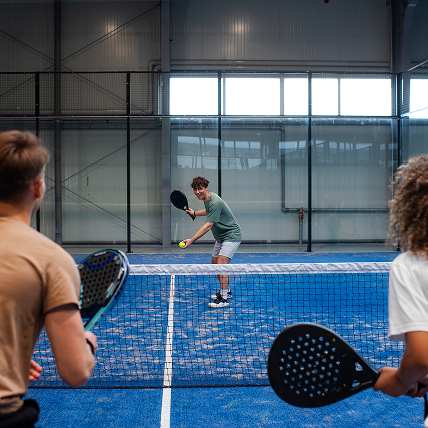 Trois joueurs en pleine partie de padel sur un terrain indoor bleu